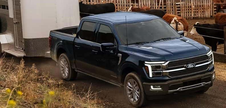 2026 Ford F-150 pickup towing a trailer near a farm, front three-quarter view