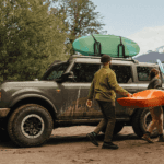 two people carrying a kayak next to a Ford Bronco
