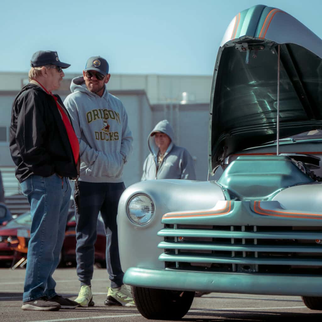 Attendees chatting beside a customized silver-and-teal vintage pickup with orange pinstriping and its hood raised at Ford of Cookeville Cars & Coffee.