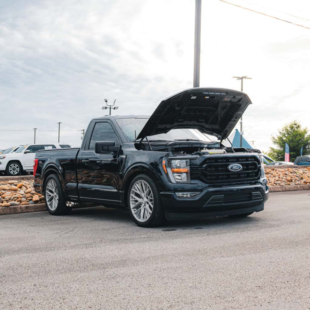 Lowered black Ford F-150 regular-cab pickup with large silver wheels and its hood raised at Ford of Cookeville Cars & Coffee.