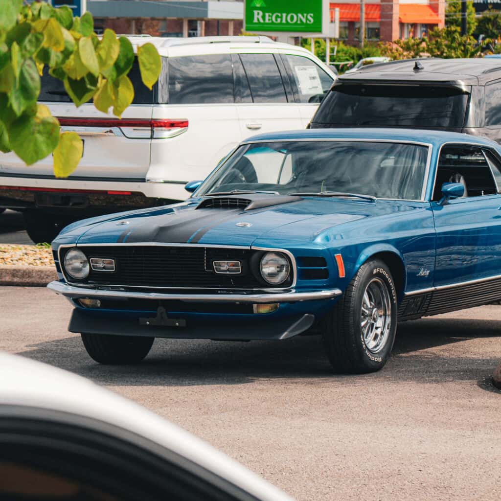 Blue classic Ford Mustang Mach 1 with black hood accents, a hood scoop, and chrome wheels parked at Ford of Cookeville Cars & Coffee.