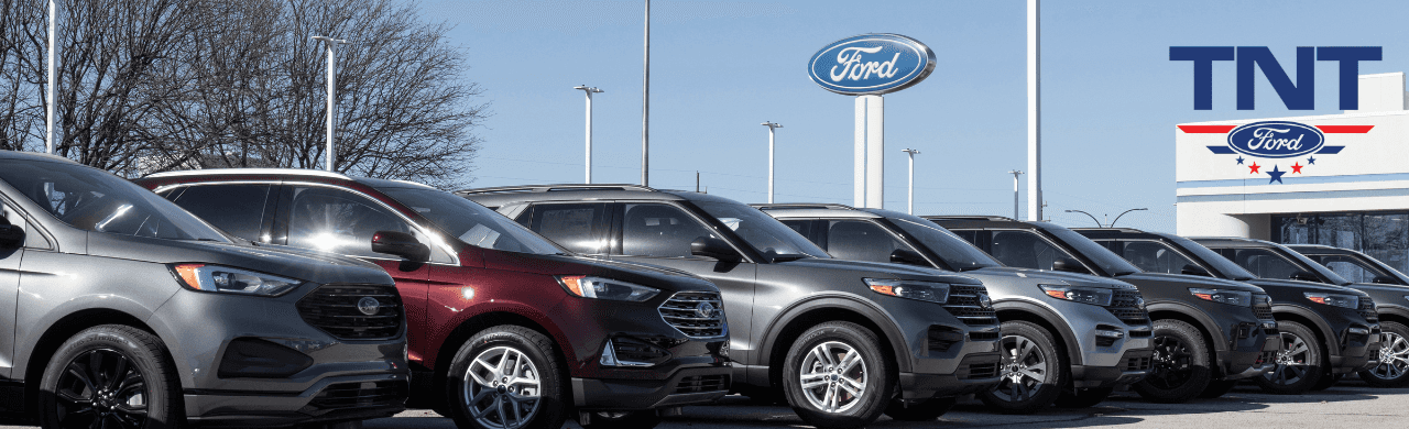 A lineup of used Ford Escape SUVs is parked outside the TNT Ford dealership in Red Oak, IA, showcasing various trims and colors available for sale.