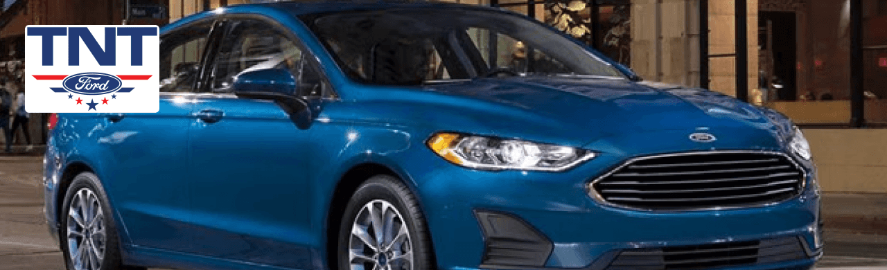 Sleek blue used Ford Fusion parked outside TNT Ford dealership in Red Oak