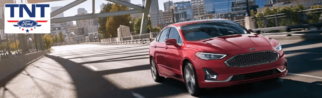 Used Ford Fusion on display at TNT Ford dealership in Red Oak, IA with a fast-sourcing banner
