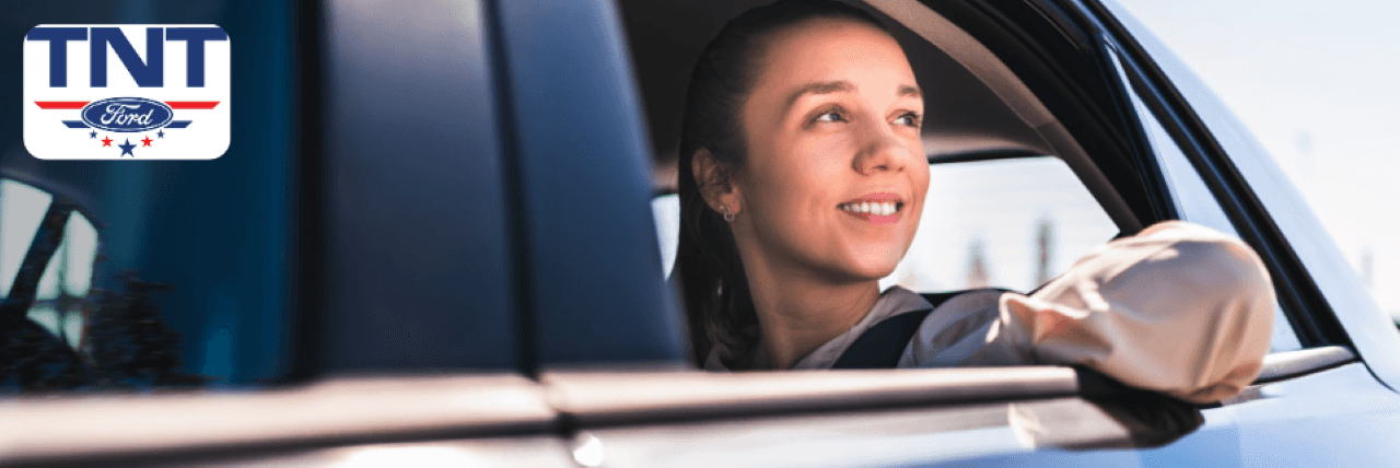 A smiling customer drives off in a newly purchased Ford SUV from TNT Ford in Red Oak, IA