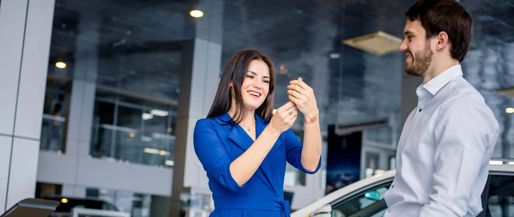 Happy beautiful woman receiving keys from a new car at auto showroom