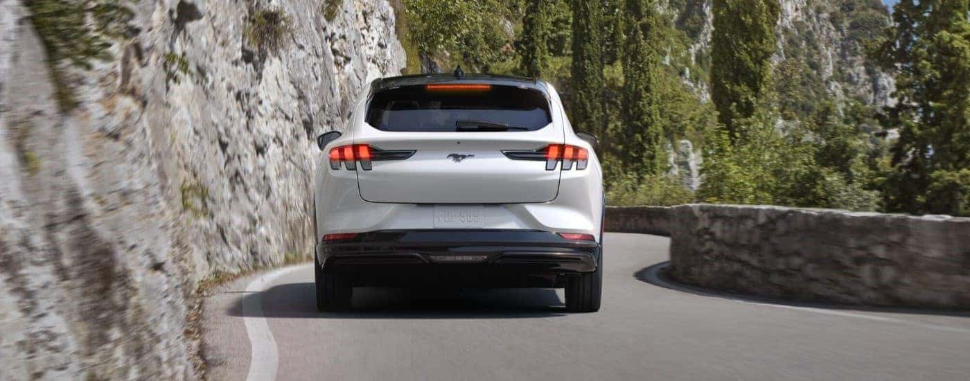 A rear view of a white 2024 Ford Mustang Mach-E driving on a mountain road.