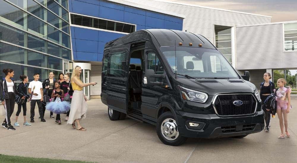 People waiting to board a black 2024 Ford Transit van.