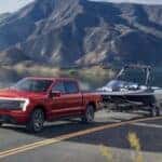 A red 2025 Ford F-150 Lightning for sale is shown towing a boat.
