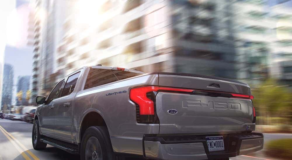 A silver 2025 Ford F-150 Lightning driving in a city.