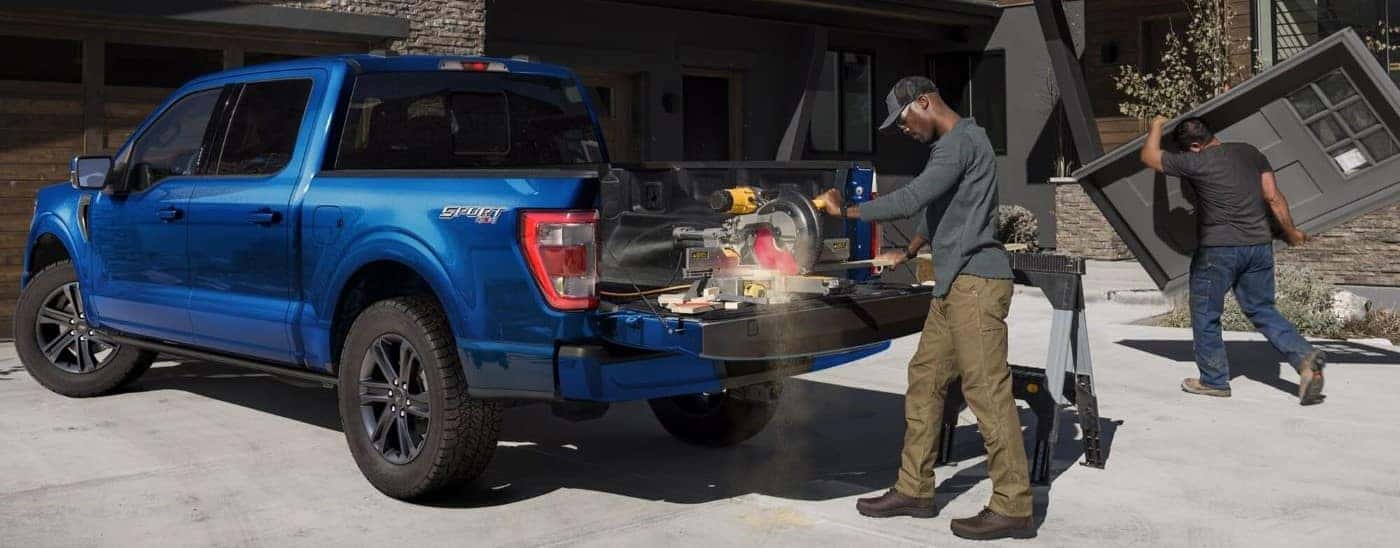 Rear view of a man operating a buzzsaw from the bed of a blue 2024 Ford F-150 Sport.
