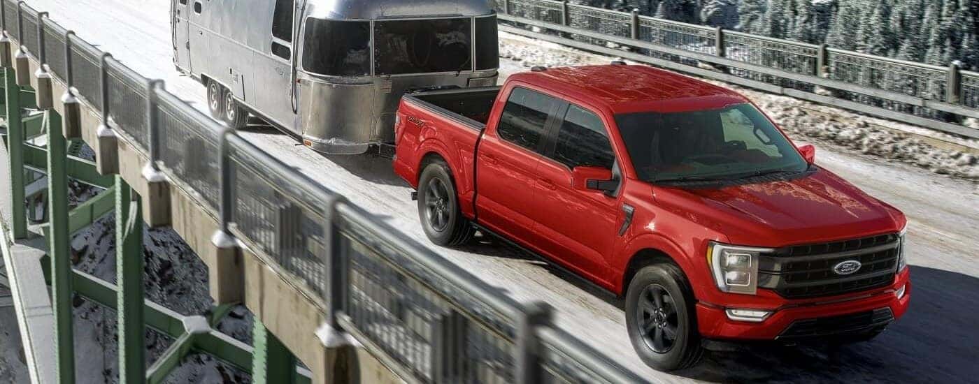 A red 2024 Ford F-150 Sport towing an Airstream camper.
