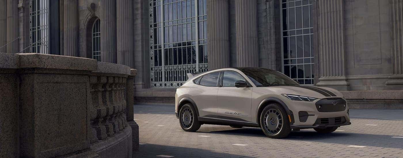 A grey 2025 Ford Mustang Mach-E Rally is parked outside of a city building.