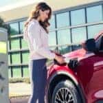 A person charging a red 2023 Ford Escape Hybrid after looking at used EVs for sale.