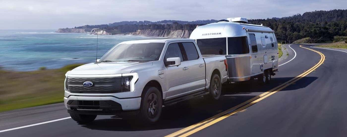 A white 2022 Ford F-150 Lightning towing a trailer after viewing used EVs for sale.