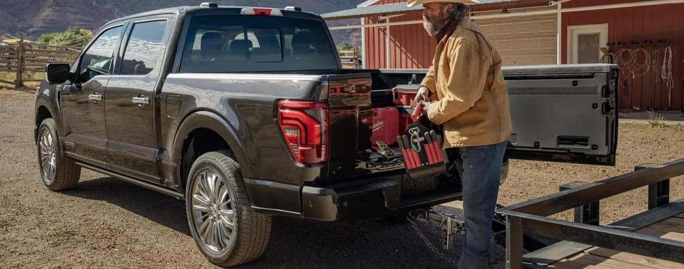 A man loading gear into the bed of a black 2024 Ford F-150 for sale.