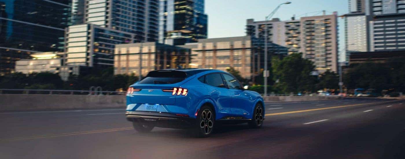 A blue 2024 Ford Mustang Mach-E driving through a city.