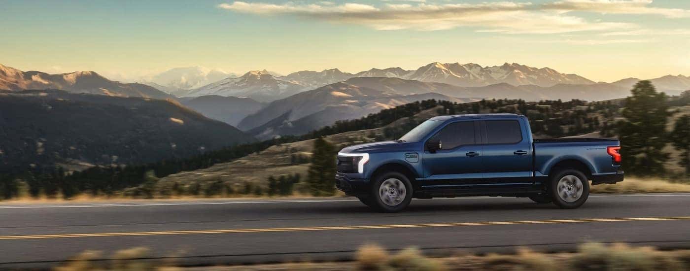 A blue 2025 Ford F-150 Lightning for sale near Watsonville driving past mountains.