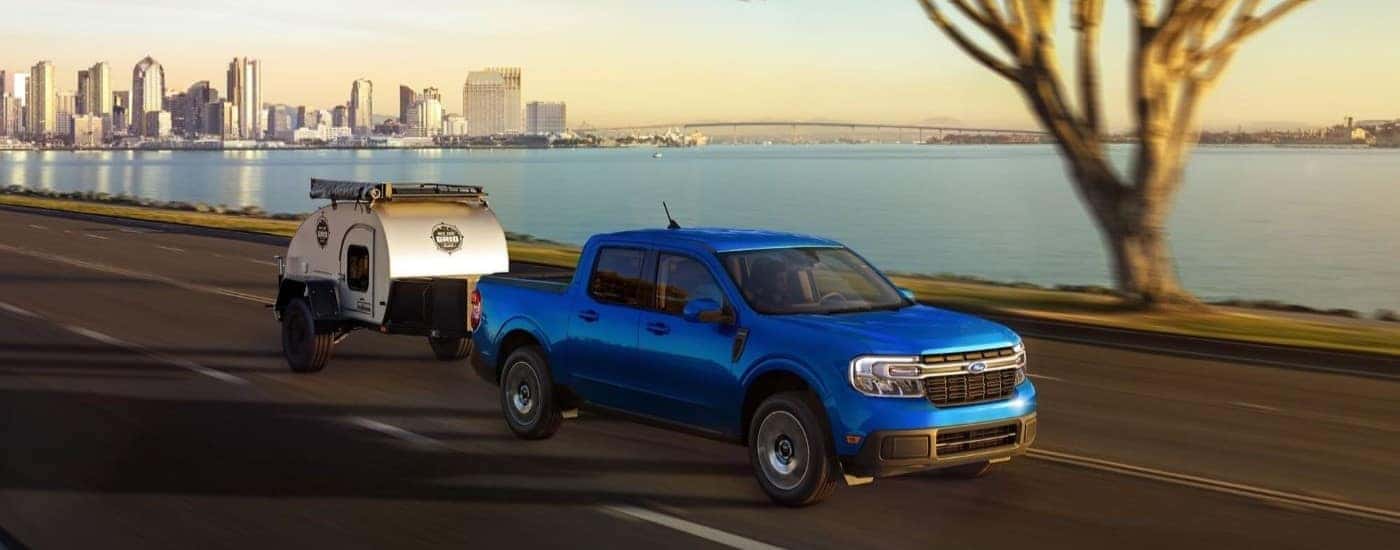 Blue 2023 Ford Maverick towing a pop-up camper along the water.