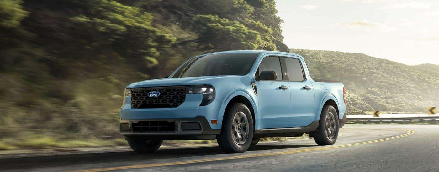Blue 2026 Ford Maverick driving on a winding road near a lake