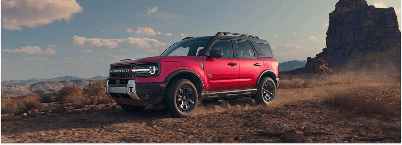 Front three-quarter view of a red 2026 Ford Bronco Sport driving on a dusty desert trail.