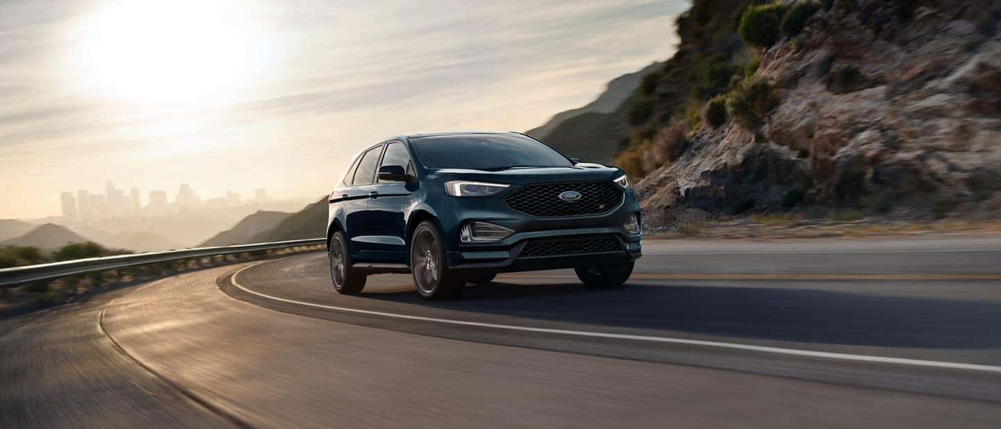 A blue Ford Edge driving on the highway next to a rocky hill