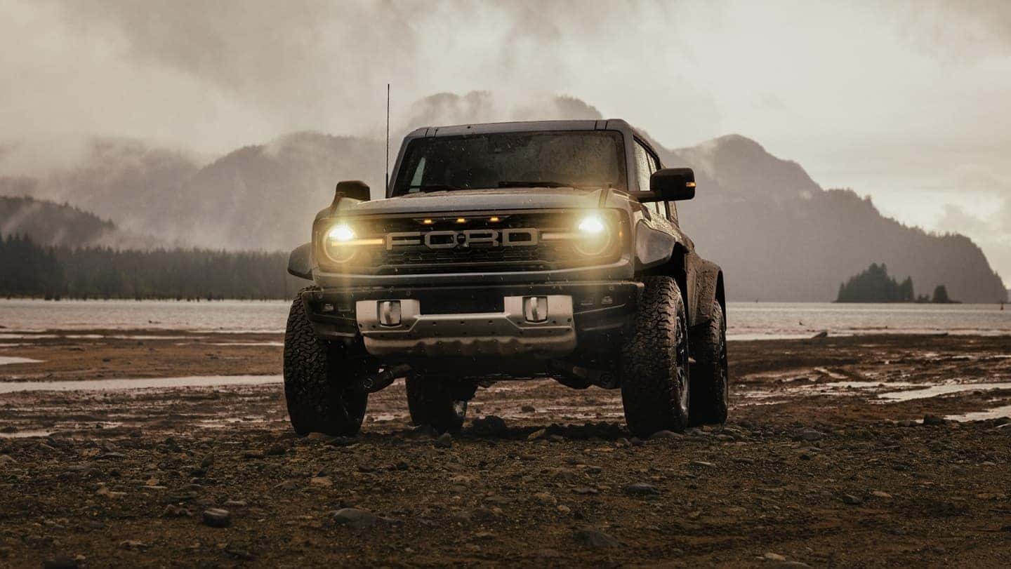 A 2025 Ford Bronco driving over dirt with its headlights on