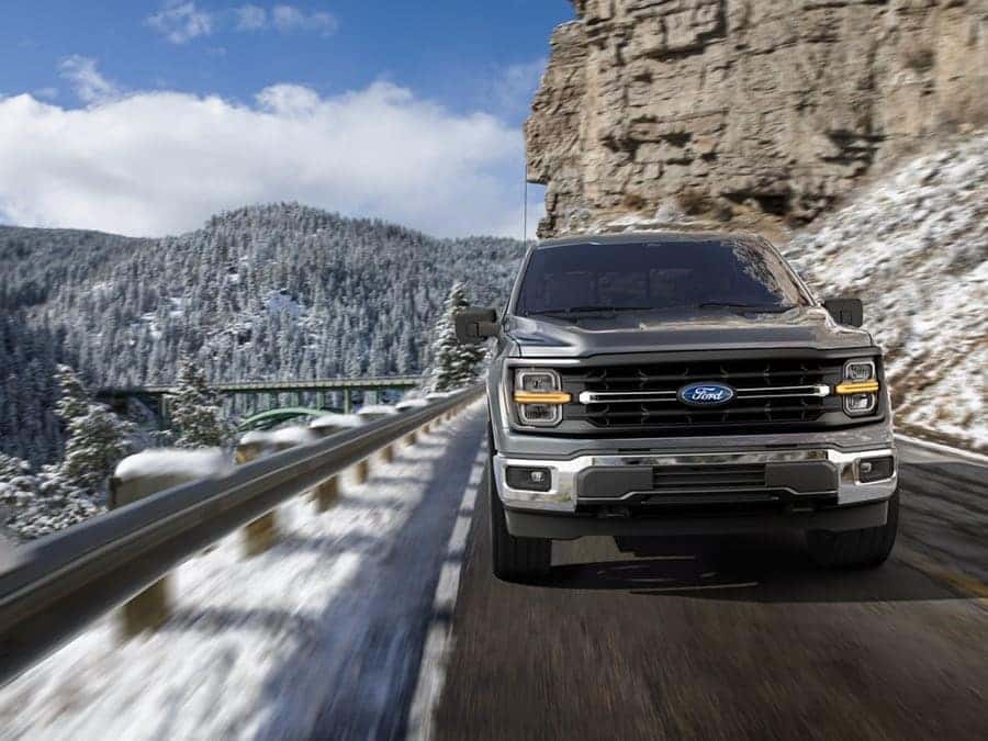 A black Ford F-150 driving down a road off a cliffside covered in snow