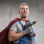 Man in coveralls wearing cape with power drill