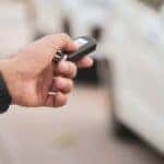 Man offering key fob in his outstretched hand with car in background