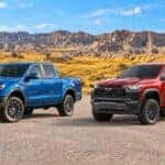 Blue 2026 Ford Ranger beside a red 2026 Chevrolet Colorado in a South Dakota landscape