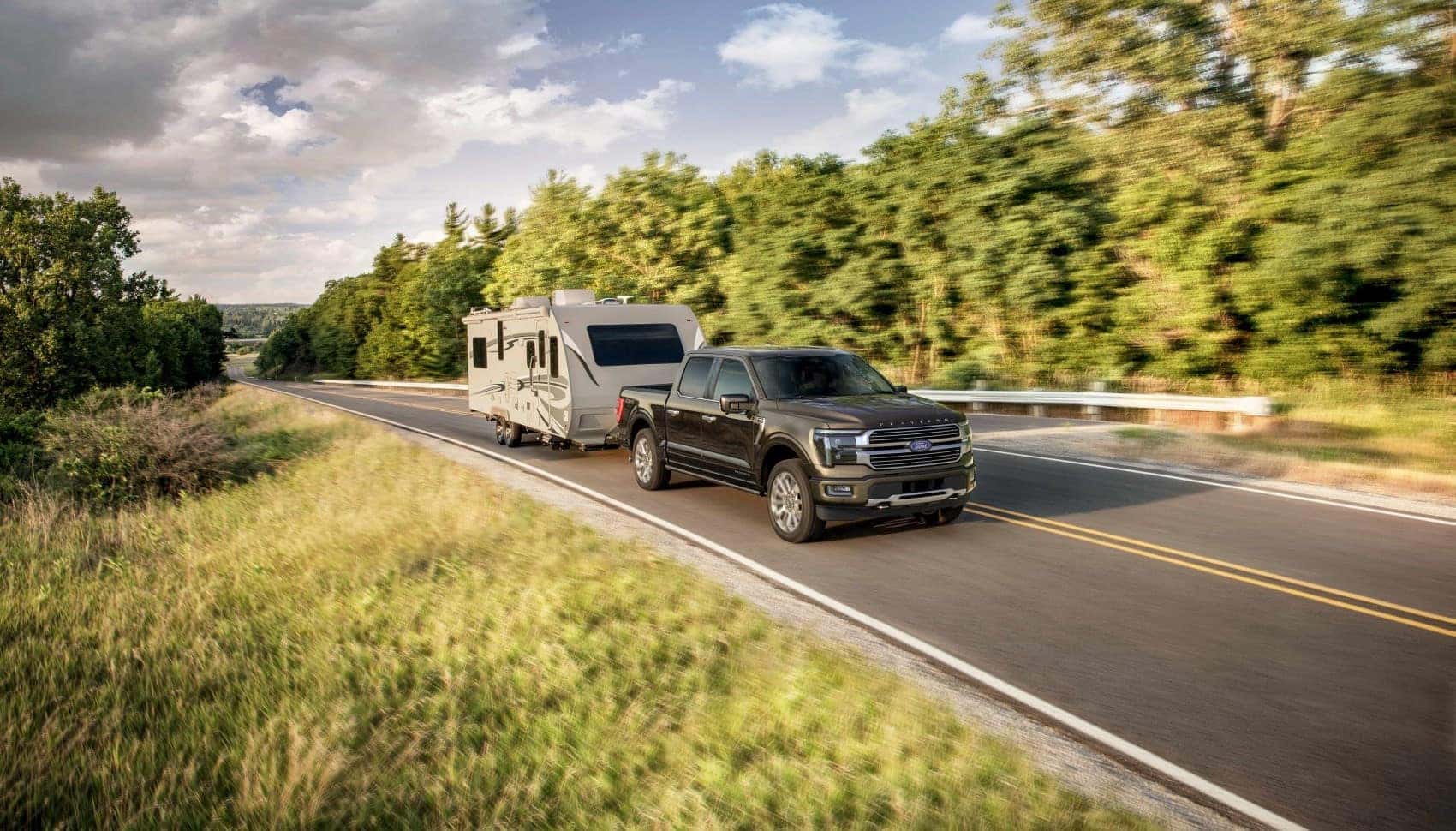 Ford Super Duty driving on scenic road with a trailer hitched to the back - Ford Dealer near Wolcott CT