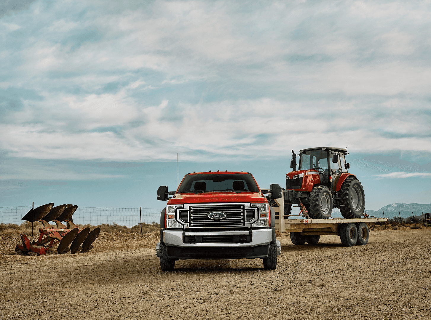 Front view of Ford Super Duty truck parked on dirt road with tractor hitched to tow