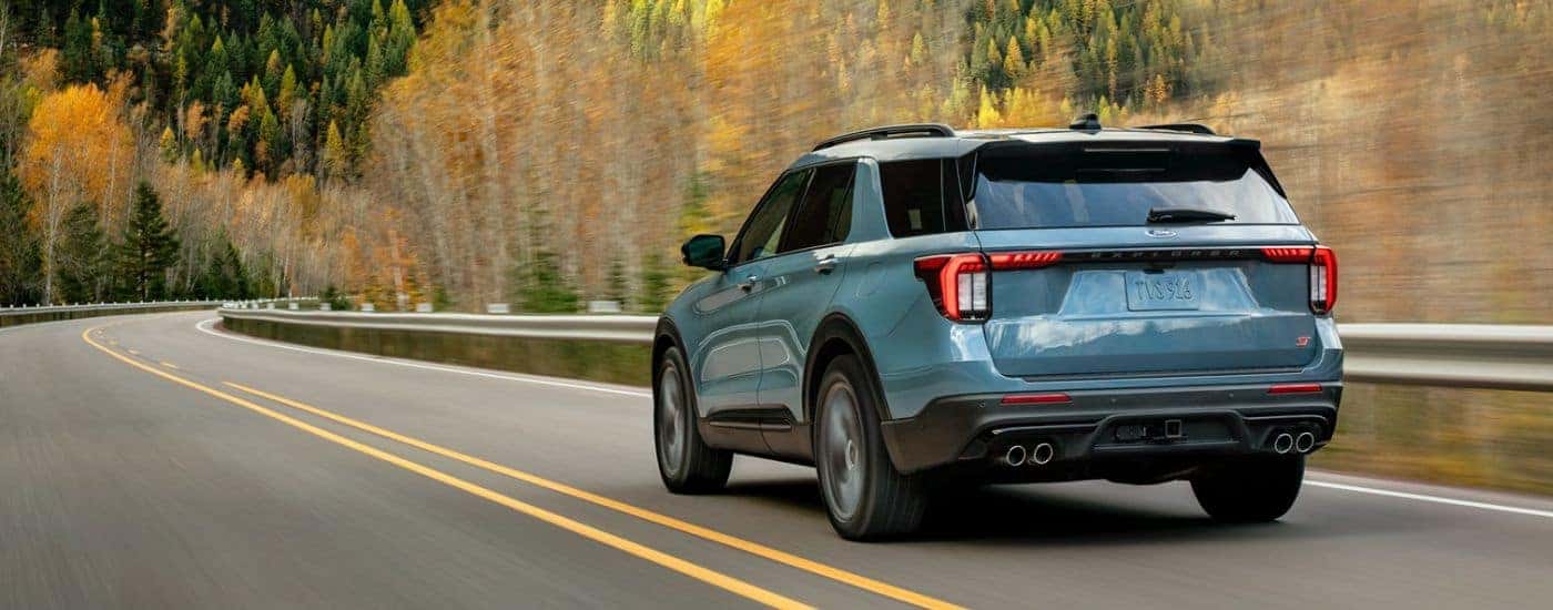 Blue 2026 Ford Explorer rear view driving down a tree lined road