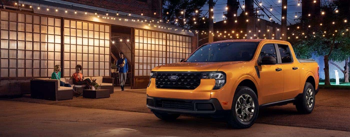 An orange 2026 Ford Maverick parked at night under string lights.