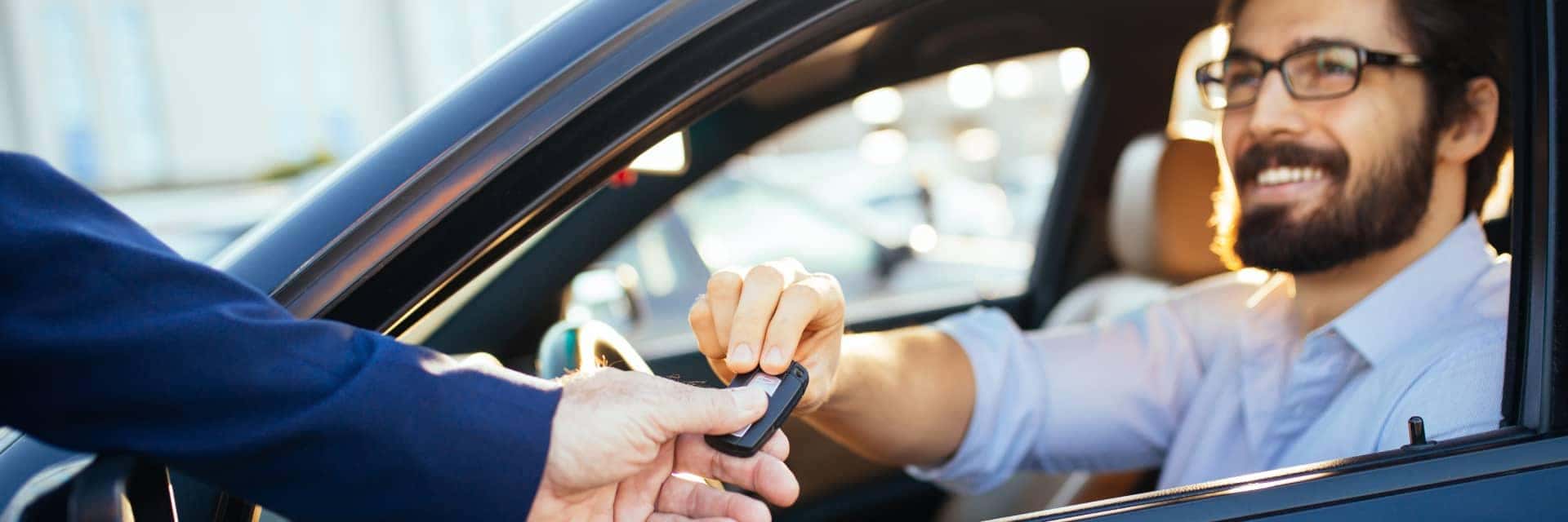 Male driver exchanging keys with sales person while sitting in vehicle