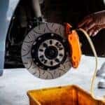 Mechanic bleeding brake fluid from an orange performance caliper on a slotted disc rotor.