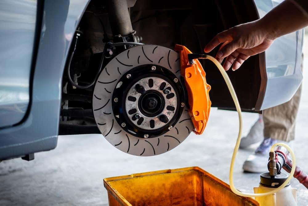 Mechanic bleeding brake fluid from an orange performance caliper on a slotted disc rotor.
