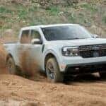 A white Ford Maverick is kicking up dirt as it drives off road.